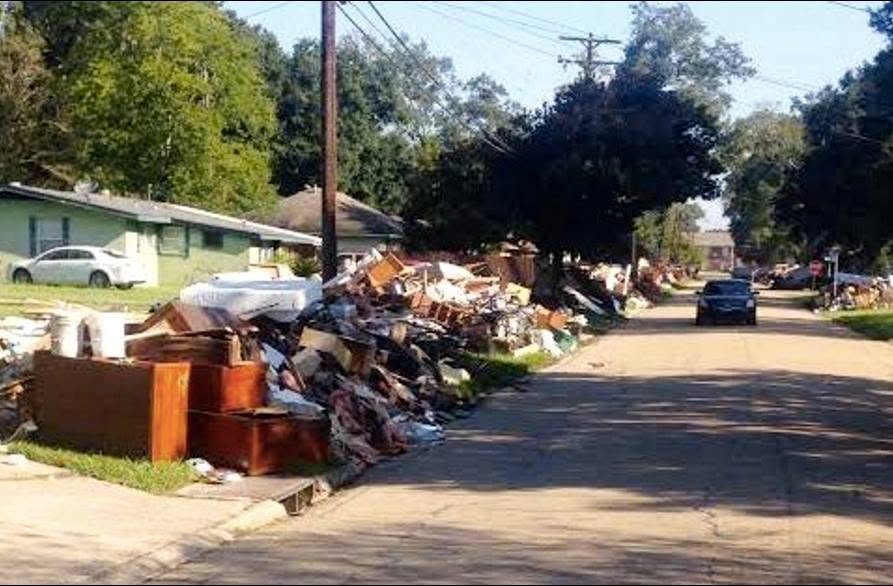 Piles of flood-ruined furniture, drywall, and family belongings stacked shoulder-high along residential curbs in Baton Rouge, Louisiana.