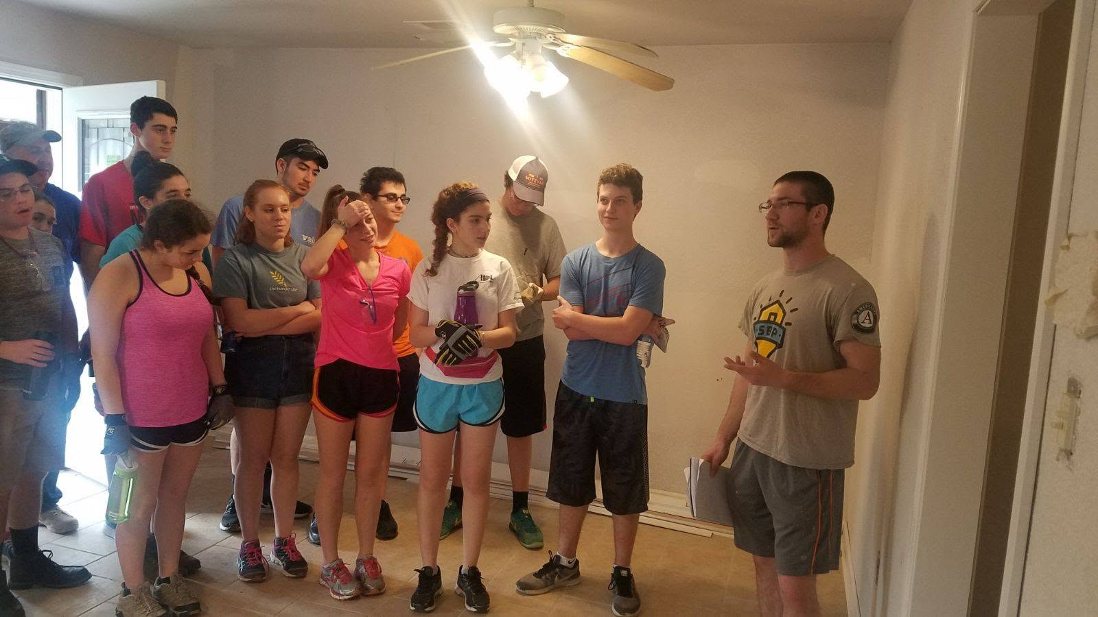 Morning construction and safety briefing led by an SBP (St. Bernard Project) AmeriCorps supervisor inside a home under reconstruction.